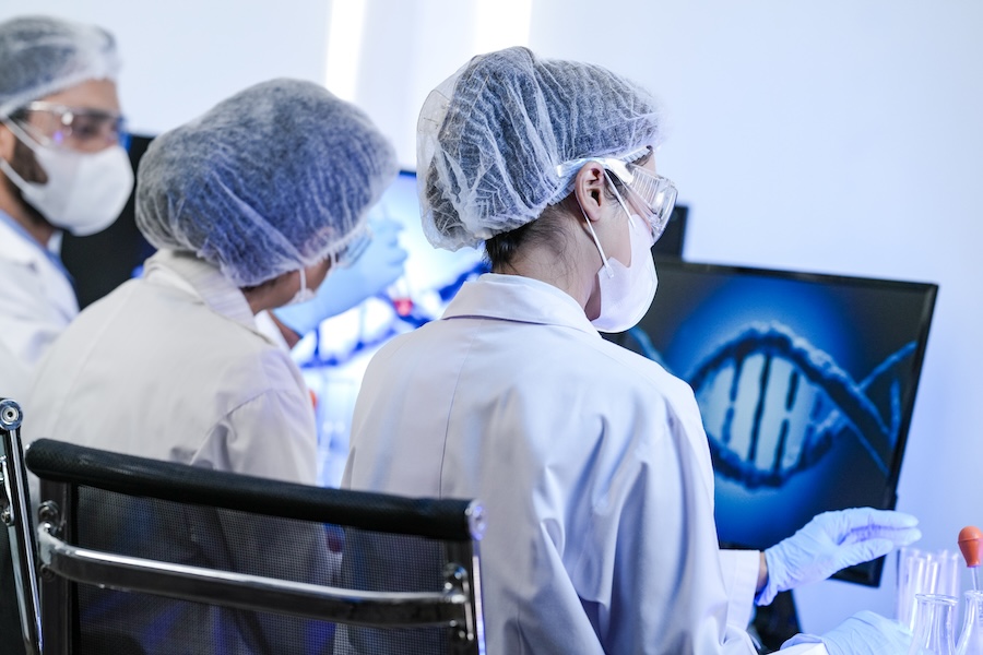 A team of scientists in a modern laboratory meticulously works on an experiment, pipetting a red liquid into a test tube next to a microscope, focused on medical research and analysis.